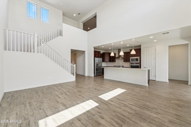 22987 E Pummelos Rd, Queen Creek, AZ 85142 - unfurnished living room with visible vents, baseboards, light wood finished floors, recessed lighting, and stairs