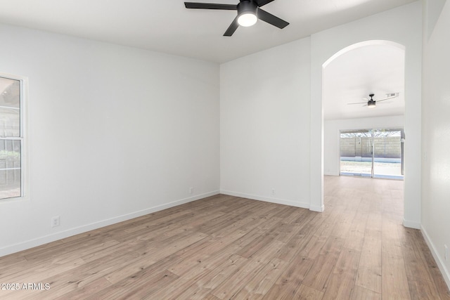 empty room with light wood-type flooring, baseboards, a ceiling fan, and arched walkways