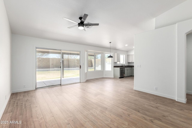 unfurnished living room with light wood-style floors, ceiling fan, baseboards, and a sink