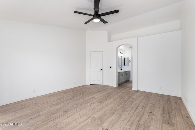 unfurnished bedroom with connected bathroom, arched walkways, lofted ceiling, light wood finished floors, and baseboards