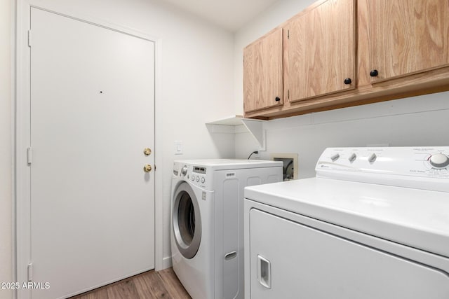 laundry room featuring washing machine and dryer, light wood-style flooring, and cabinet space