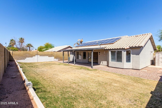 back of property with a tiled roof, a fenced backyard, solar panels, and a patio area