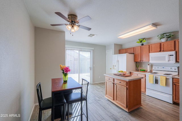 kitchen with white appliances, ceiling fan, a center island, a textured ceiling, and light wood-type flooring