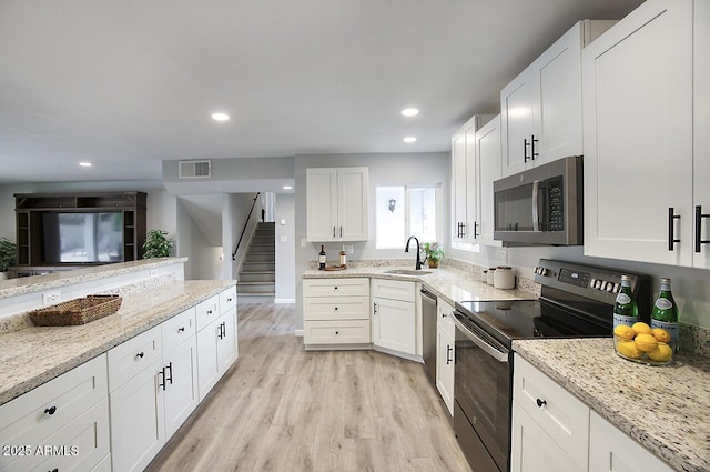 kitchen with white cabinetry, stainless steel appliances, sink, and light stone counters