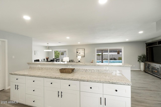 kitchen with white cabinetry, light stone counters, hanging light fixtures, light wood-type flooring, and a kitchen island