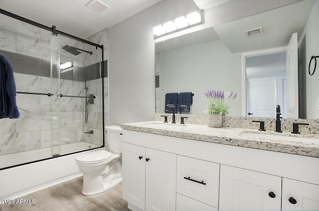 full bathroom featuring vanity, hardwood / wood-style flooring, enclosed tub / shower combo, and toilet