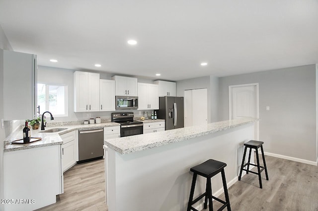 kitchen with sink, a breakfast bar area, white cabinetry, light wood-type flooring, and appliances with stainless steel finishes