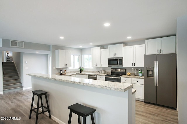 kitchen with a breakfast bar area, stainless steel appliances, light stone countertops, light hardwood / wood-style floors, and white cabinets