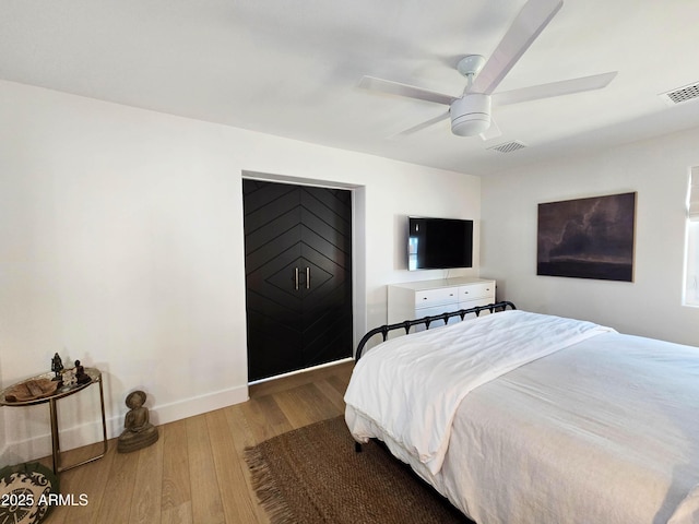 bedroom featuring a ceiling fan, wood finished floors, visible vents, and baseboards