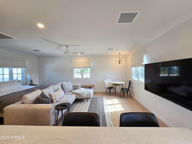 living area with ceiling fan with notable chandelier, light wood finished floors, visible vents, and baseboards