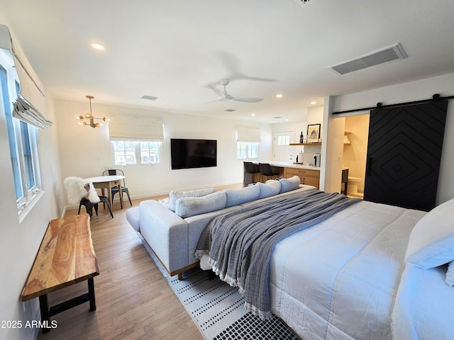 bedroom featuring a barn door, visible vents, light wood-style flooring, and recessed lighting