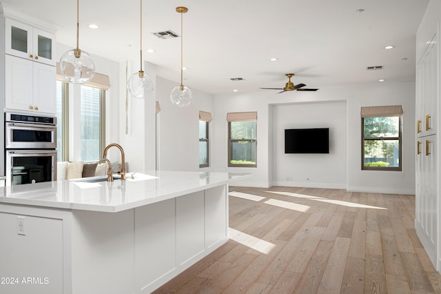 kitchen featuring a wealth of natural light, white cabinets, stainless steel double oven, and light wood-type flooring