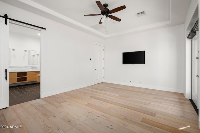 unfurnished room featuring ceiling fan, a barn door, a raised ceiling, and light hardwood / wood-style flooring