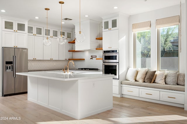 kitchen with a kitchen island with sink, white cabinets, light hardwood / wood-style flooring, decorative light fixtures, and stainless steel appliances