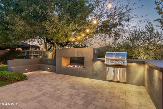 patio terrace at dusk with a tile fireplace, area for grilling, and a grill