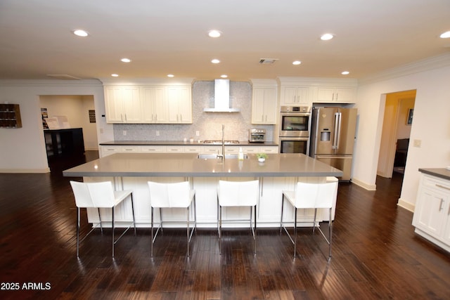 kitchen with wall chimney exhaust hood, crown molding, a large island with sink, white cabinets, and appliances with stainless steel finishes