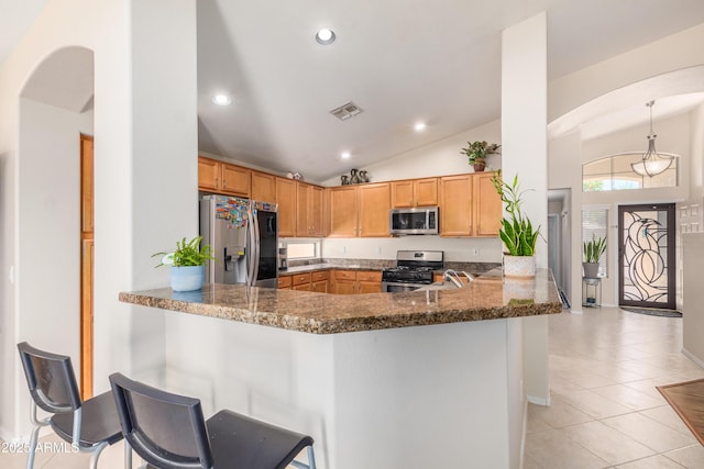 kitchen with light tile patterned floors, a breakfast bar, dark stone countertops, stainless steel appliances, and kitchen peninsula