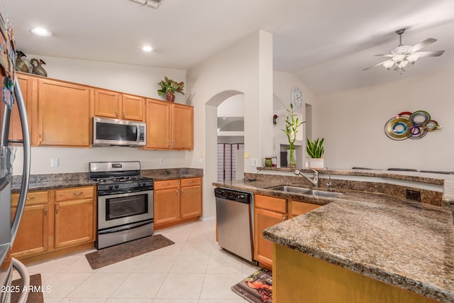 kitchen featuring lofted ceiling, sink, light tile patterned floors, appliances with stainless steel finishes, and dark stone countertops