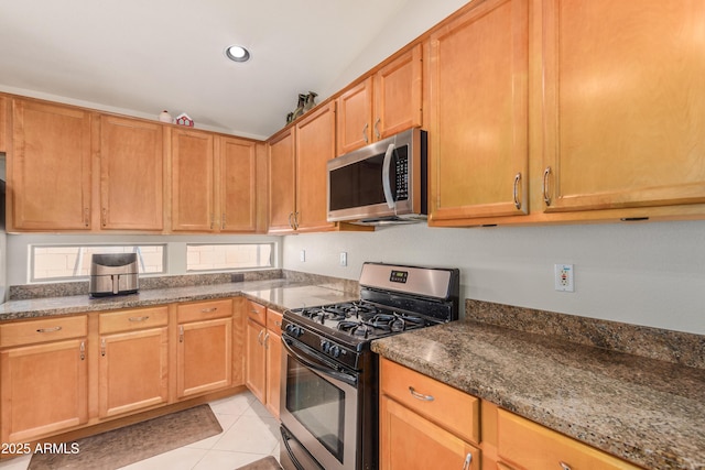 kitchen featuring appliances with stainless steel finishes, light tile patterned floors, and dark stone counters