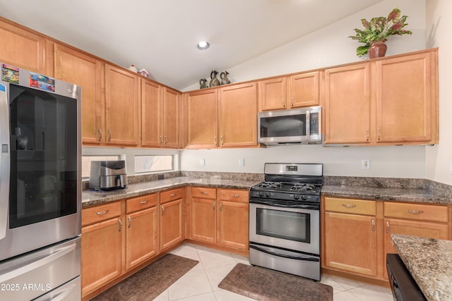 kitchen featuring lofted ceiling, light tile patterned floors, dark stone counters, and appliances with stainless steel finishes