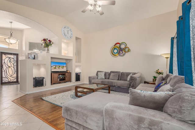 living room featuring vaulted ceiling, light tile patterned floors, built in features, and ceiling fan