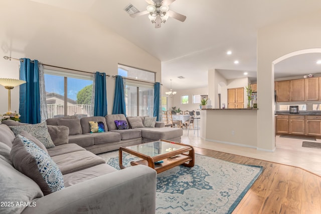 living room featuring ceiling fan with notable chandelier, a wealth of natural light, high vaulted ceiling, and light wood-type flooring