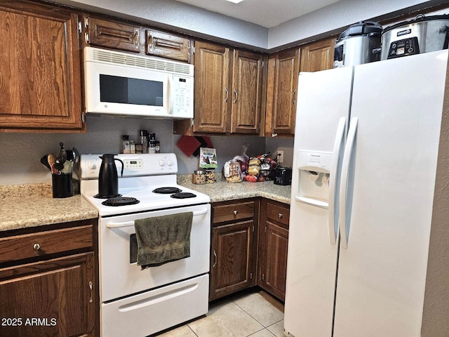 kitchen with dark brown cabinets, light tile patterned floors, and white appliances