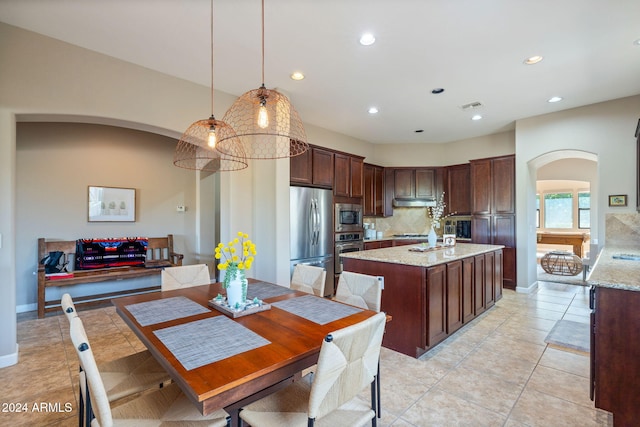 kitchen with light stone countertops, hanging light fixtures, decorative backsplash, light tile patterned floors, and appliances with stainless steel finishes