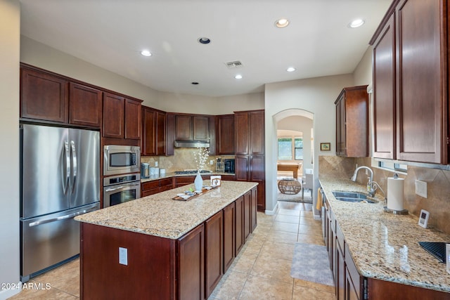 kitchen featuring a center island, light stone counters, backsplash, and appliances with stainless steel finishes