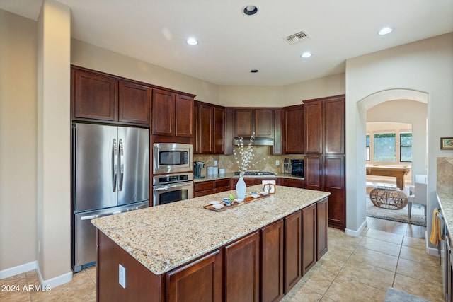 kitchen featuring a center island, decorative backsplash, light tile patterned floors, appliances with stainless steel finishes, and light stone counters