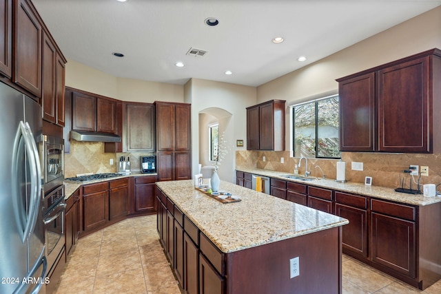 kitchen featuring tasteful backsplash, light stone counters, a kitchen island, and stainless steel appliances