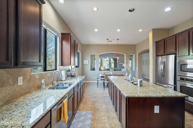 kitchen with light stone countertops, stainless steel appliances, tasteful backsplash, decorative light fixtures, and a kitchen island