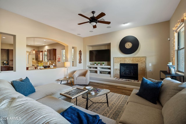 living room featuring a tile fireplace, wood-type flooring, and ceiling fan