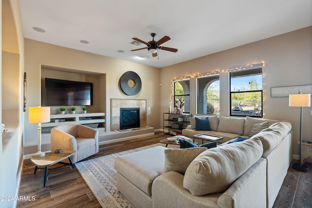 living room with a tiled fireplace, ceiling fan, and dark hardwood / wood-style flooring