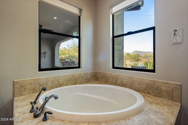 bathroom featuring plenty of natural light, a relaxing tiled tub, and a mountain view