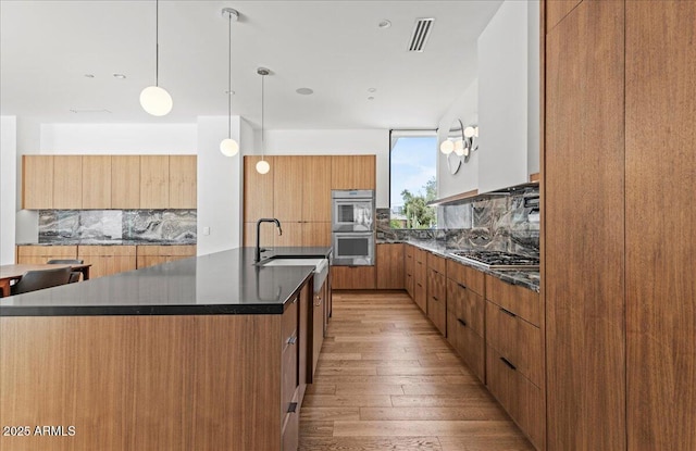 5301 N 43rd St, Phoenix, AZ 85018 - kitchen with modern cabinets, appliances with stainless steel finishes, decorative backsplash, an island with sink, and light wood finished floors