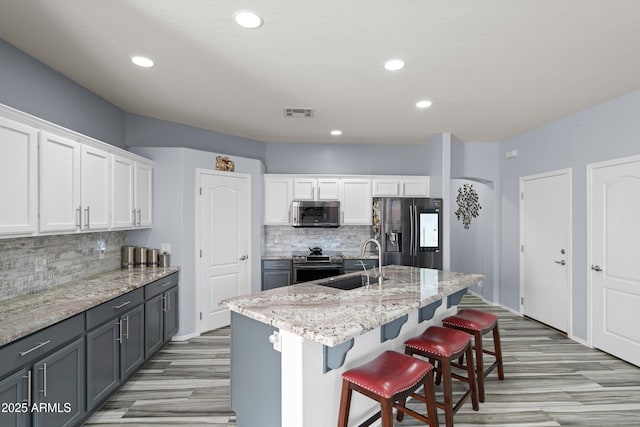 kitchen with gray cabinetry, white cabinets, sink, an island with sink, and appliances with stainless steel finishes