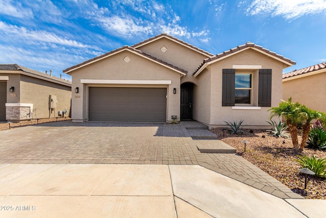 ranch-style house with a garage, stucco siding, a tile roof, and decorative driveway