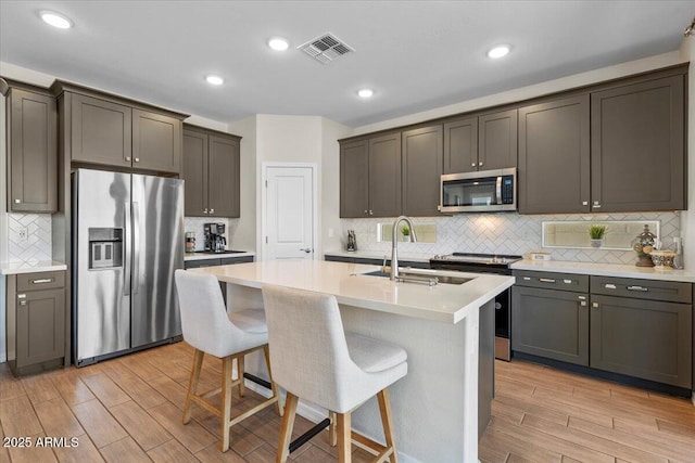 880 S 150th Dr, Goodyear, AZ 85338 - kitchen featuring stainless steel appliances, decorative backsplash, light wood finished floors, light countertops, and a breakfast bar
