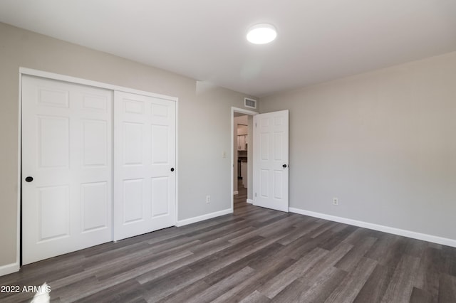 unfurnished bedroom featuring a closet, visible vents, dark wood-type flooring, and baseboards