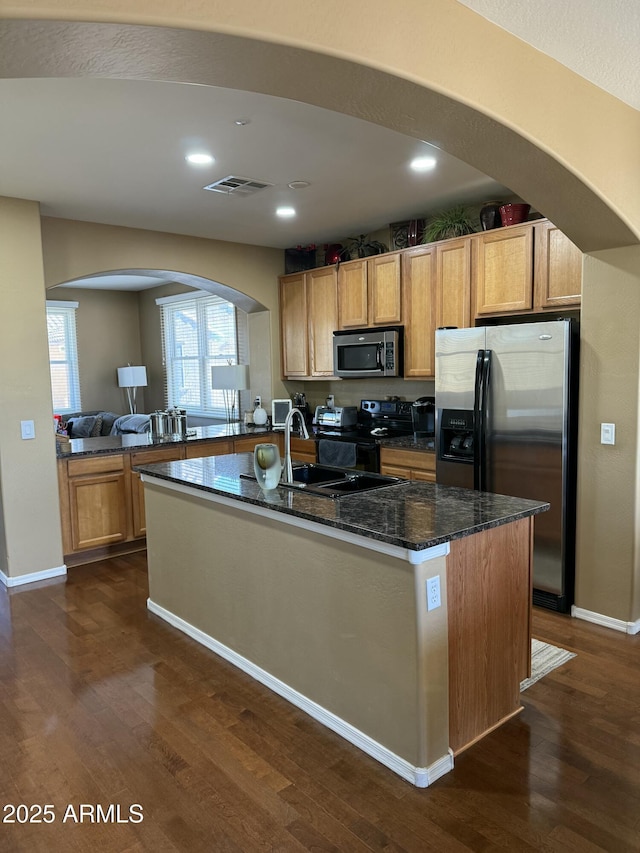 kitchen featuring dark stone countertops, a center island with sink, stainless steel appliances, and dark hardwood / wood-style floors