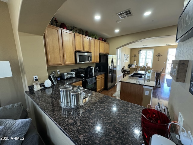 kitchen featuring sink, stainless steel appliances, kitchen peninsula, dark stone counters, and decorative light fixtures