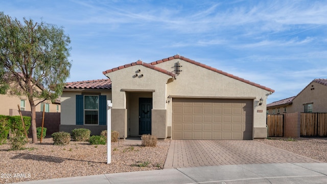 mediterranean / spanish home featuring a garage, fence, a tiled roof, decorative driveway, and stucco siding