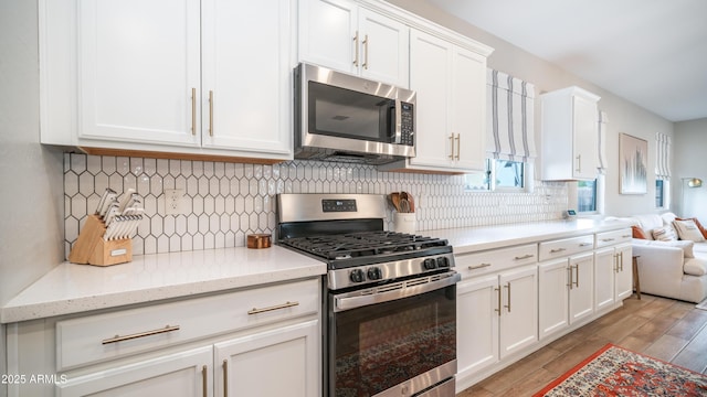 kitchen featuring stainless steel appliances, backsplash, light wood-style flooring, white cabinetry, and light stone countertops