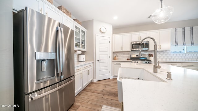 kitchen featuring white cabinets, light wood-style flooring, appliances with stainless steel finishes, light countertops, and backsplash