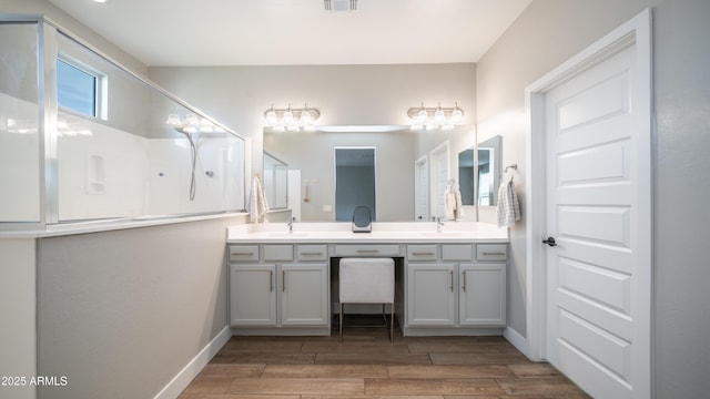 bathroom with wood finish floors, a sink, visible vents, baseboards, and double vanity