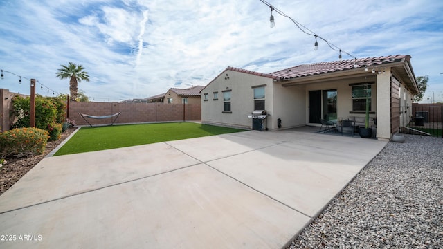 rear view of house with a patio, a tile roof, a fenced backyard, a yard, and stucco siding