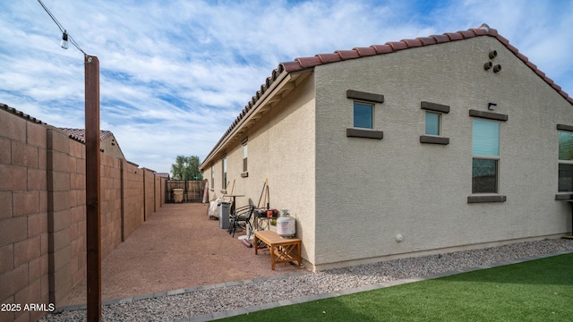 view of side of home featuring a tile roof, a patio area, a fenced backyard, and stucco siding