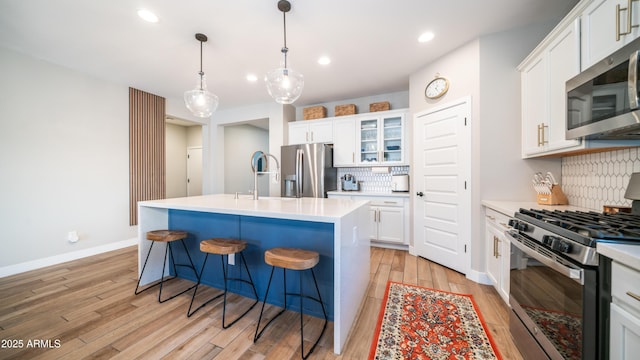 kitchen featuring stainless steel appliances, white cabinetry, a kitchen breakfast bar, light wood-style floors, and a center island with sink