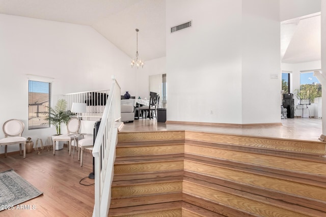 staircase with wood-type flooring, plenty of natural light, a notable chandelier, and high vaulted ceiling